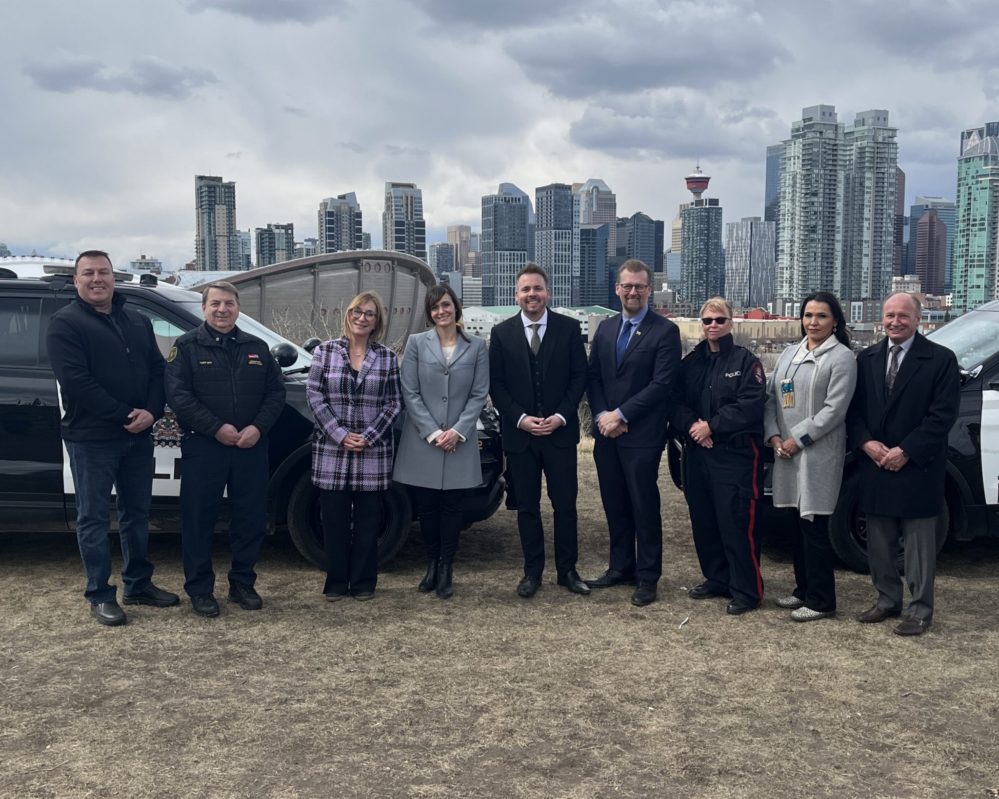 Councillor Sharp and members of the Public Safety and Community Response Task Force in front of police vehicles, with the Calgary skyline in the background