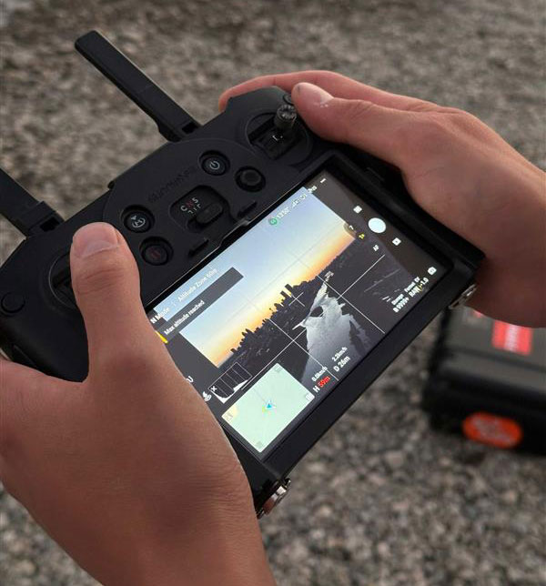 Person holding drone controls with screen showing drone image.