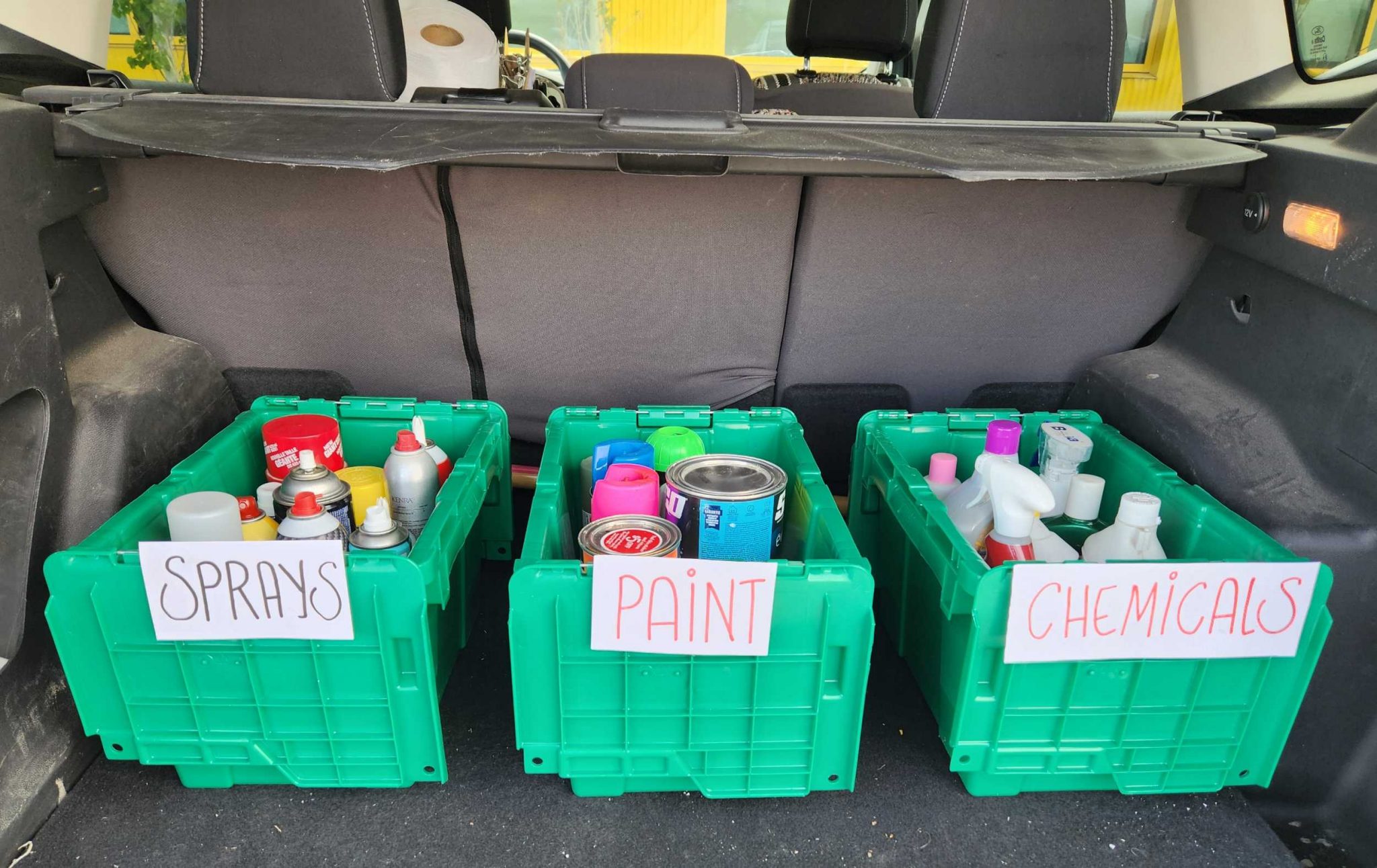 Three bins marked sprays, paint and chemicals in the back of a car for transportation.