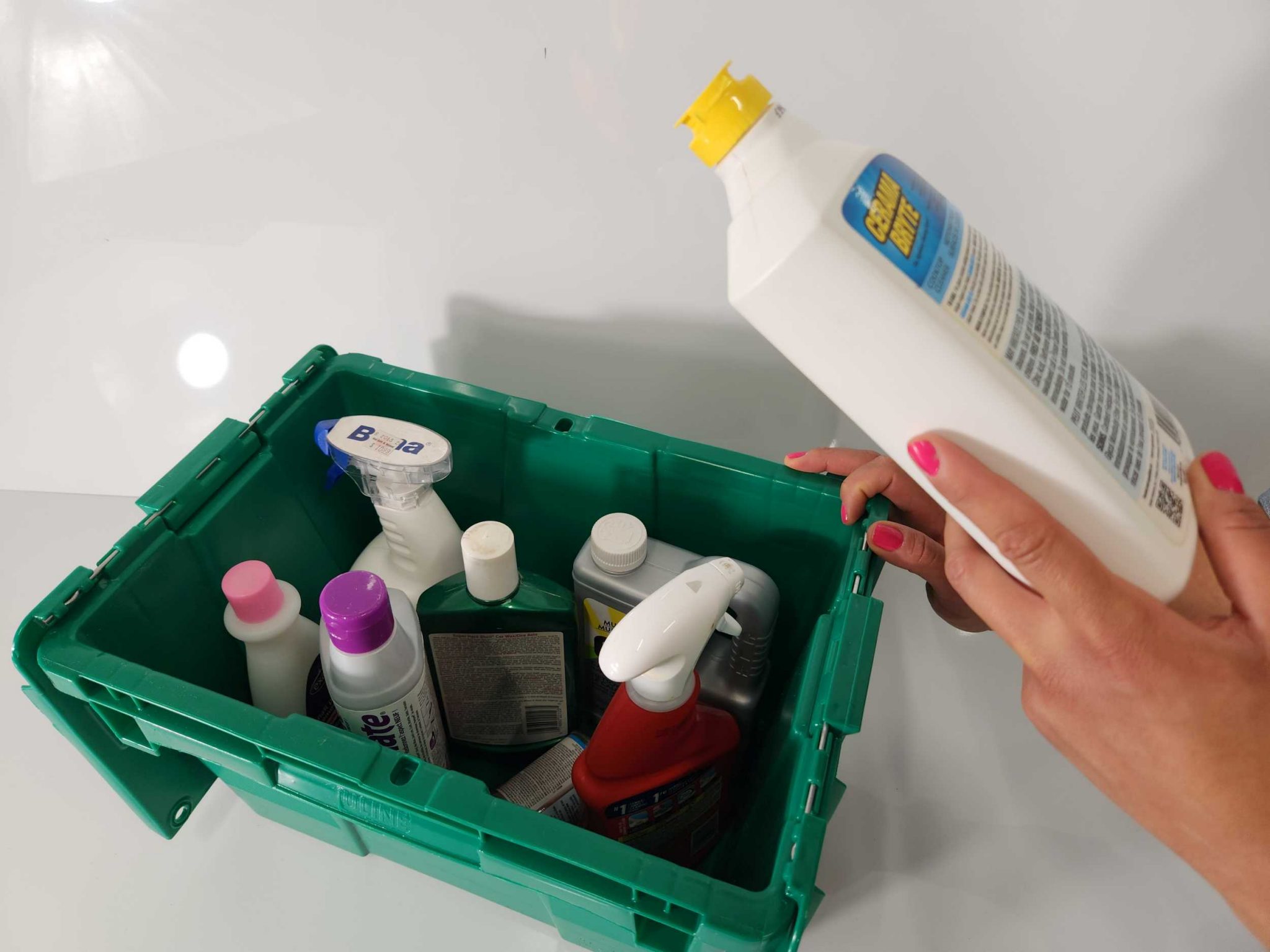 Person holding and reading label on a chemical bottle, with other chemical bottles in a green bucket.