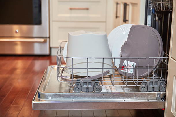 A dishwasher open with the bottom racked pulled out and a compost kitchen pail on the rack.