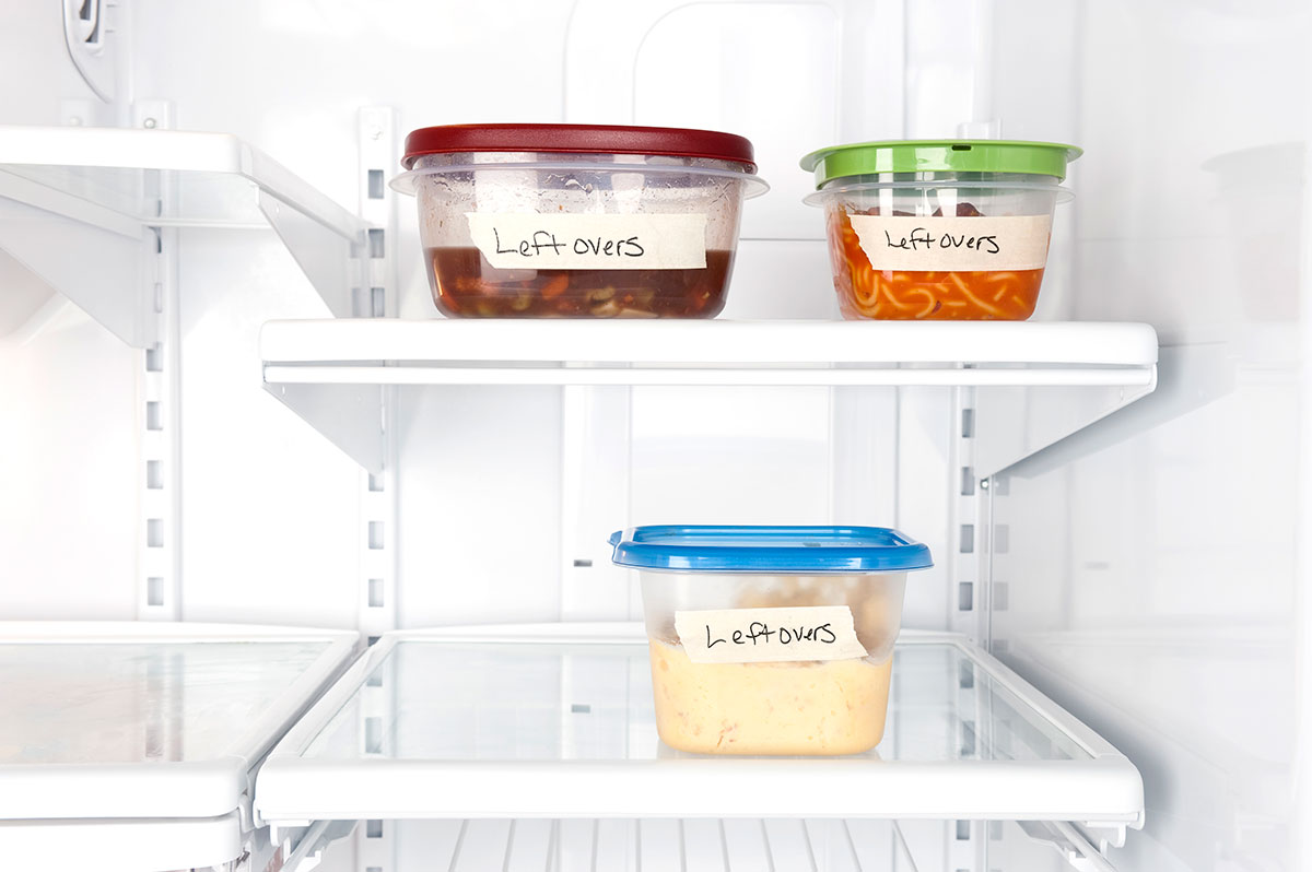 View of inside of a fridge with 2 containers on the top shelf and 1 container on the bottom shelf all with the label "leftovers".