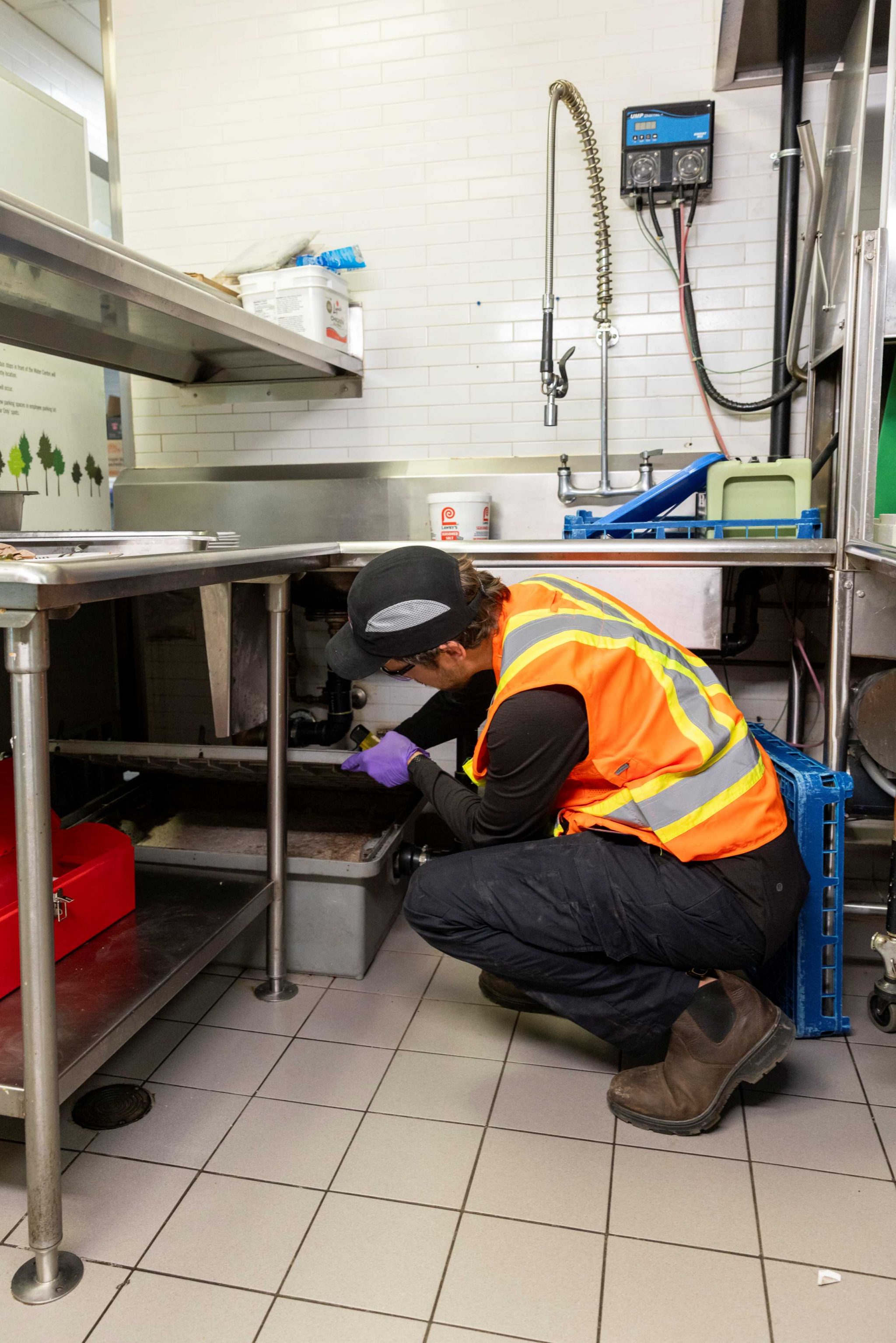 A person wearing a safety vest checking a grease interceptor (grease trap).